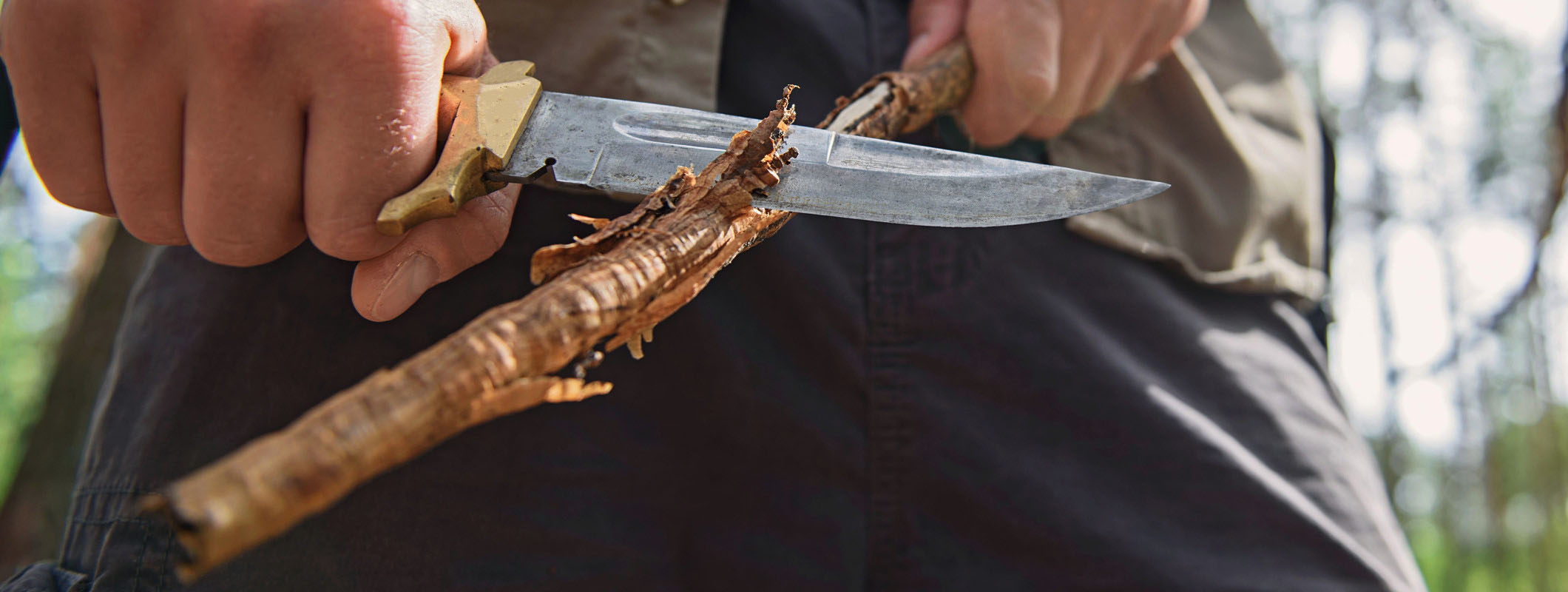 Hand-forged bushcraft knife carving wood in the field, showing the fine control a short Scandi-ground fixed blade gives