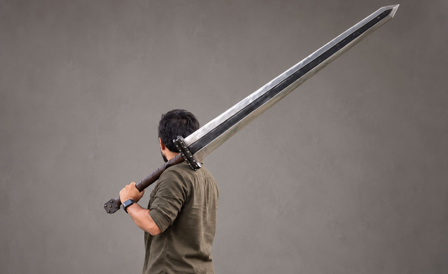 Hand-forged Guts Raider greatsword in dark forge finish, blackened flats with bright polished bevels, carried on the shoulder in the studio