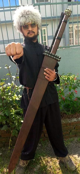 Hand-forged Guts Raider greatsword in its brown leather scabbard, held upright to show the full size against a man