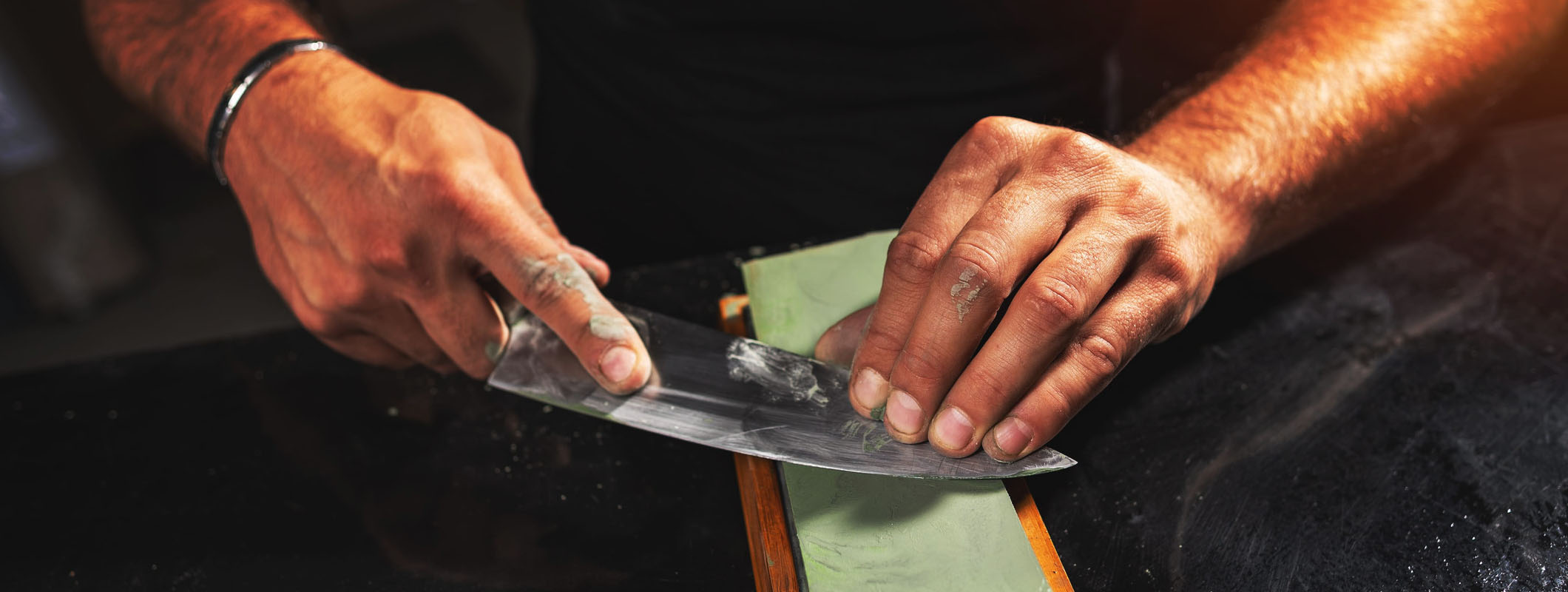 Sharpening a carbon steel chef knife on a whetstone at a low angle - hand-forged kitchen knife care by Everest Forge
