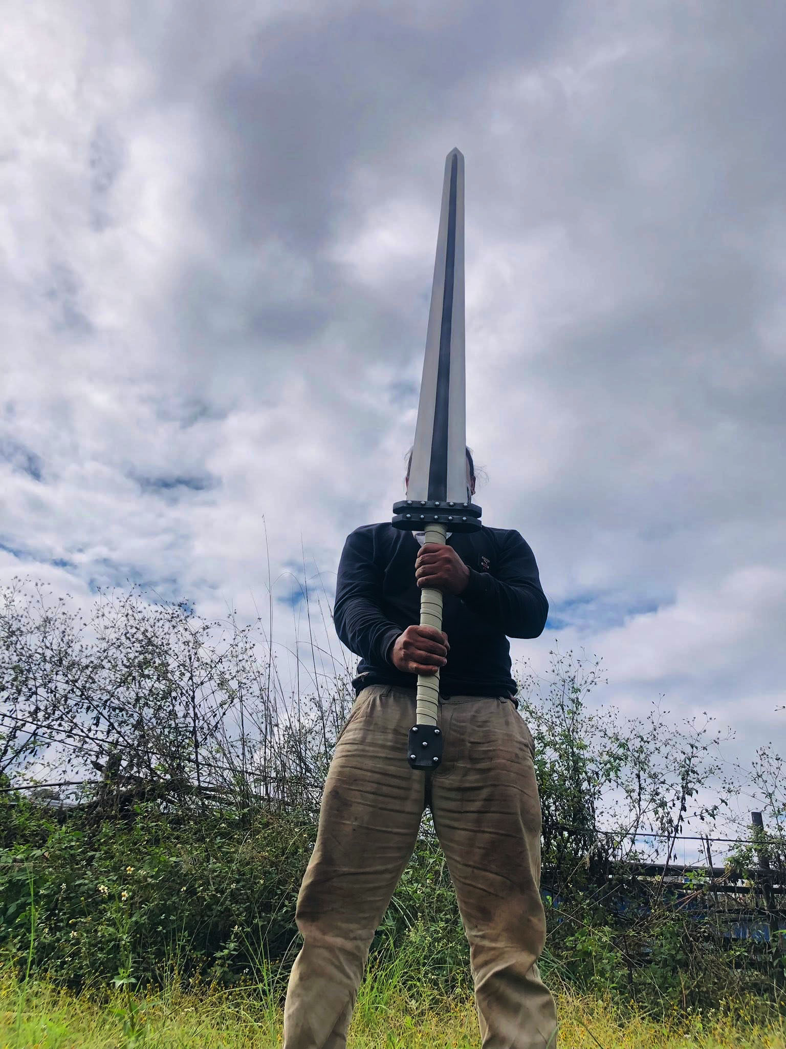 Hand-forged Golden Age Guts sword from the same forge held upright in both hands, showing full blade length